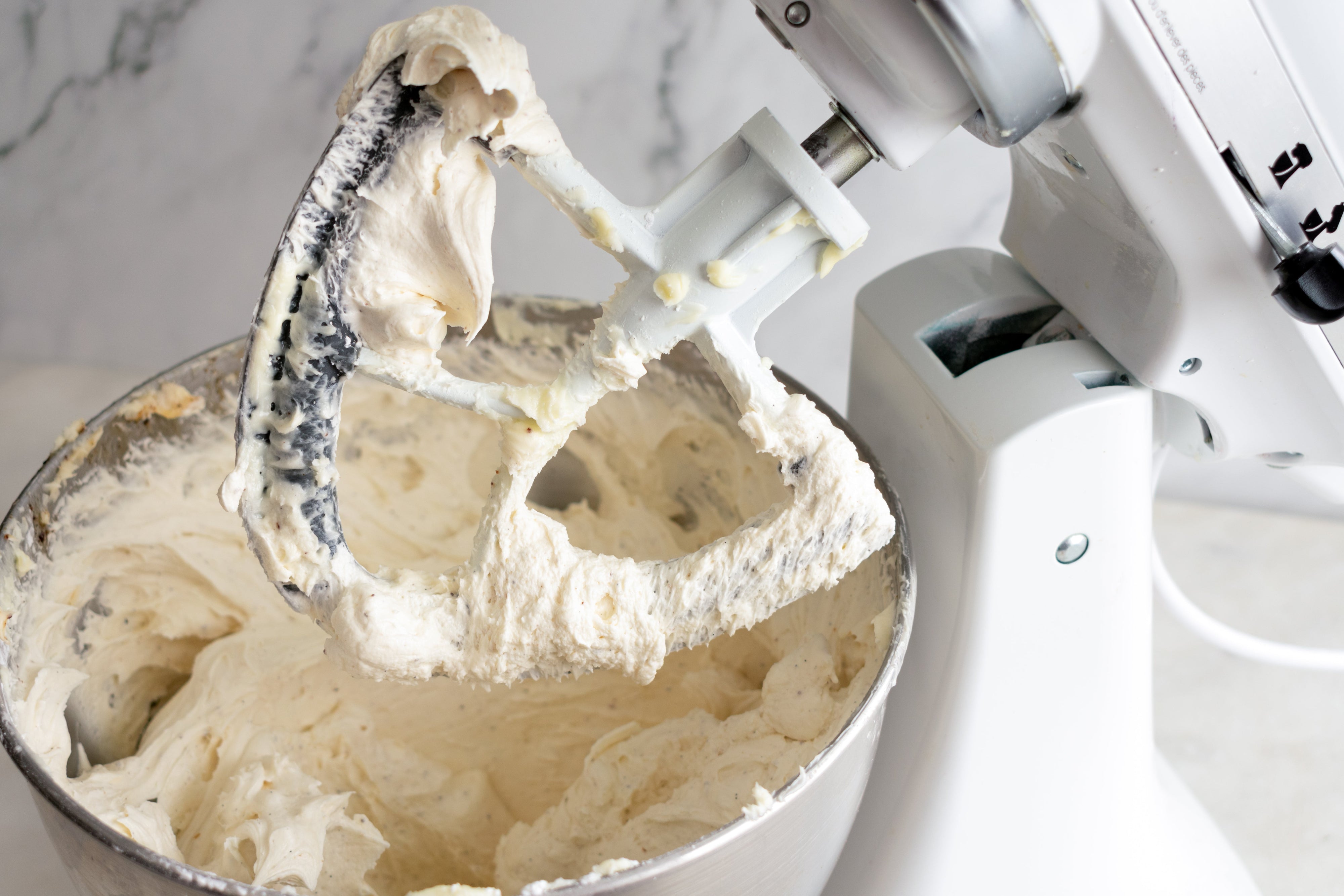 A bowl attached to a kitchen mixer filled with cream cheese frosting.